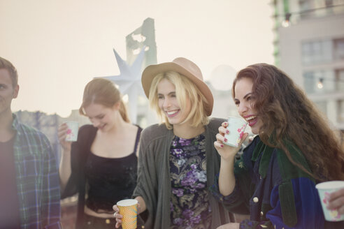 Smiling young women drinking and laughing at rooftop party - CAIF16119