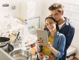 Affectionate young couple using digital tablet in apartment kitchen - CAIF16130