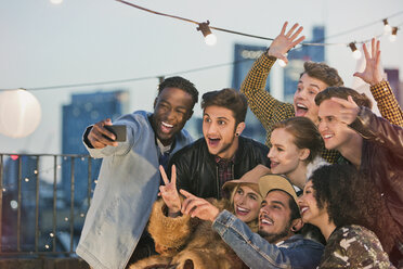 Enthusiastic young adult friends cheering and taking selfie at rooftop party - CAIF16153