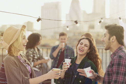 Young adult friends laughing and drinking at rooftop party - CAIF16157
