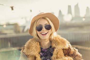 Portrait begeisterte junge Frau mit Hut und Sonnenbrille auf einem sonnigen Dach - CAIF16160