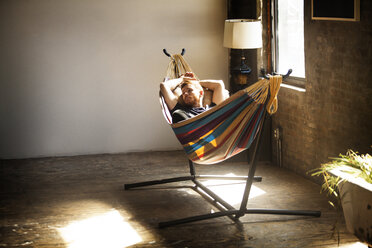 Man looking away while relaxing in hammock tied on stand at home - CAVF07894