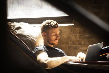 Man using laptop computer while relaxing in hammock - CAVF07895