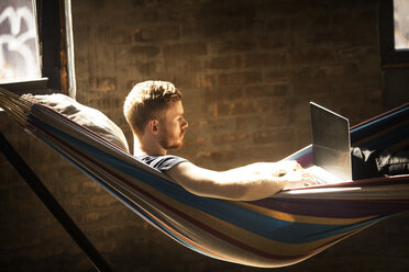 Man using laptop computer while sitting hammock at home - CAVF07896