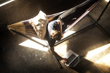 Overhead view of man using laptop computer while sitting in hammock tied on stand - CAVF07900