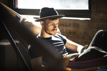 Mann mit Hut, der ein Buch liest, während er sich in der Hängematte entspannt - CAVF07907