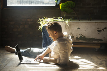 Man using laptop computer while reclining on floor at home - CAVF07919