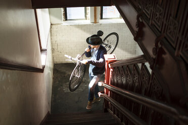 Hochformatige Ansicht eines Mannes, der ein Fahrrad trägt, während er zu Hause eine Treppe hinaufsteigt - CAVF07939