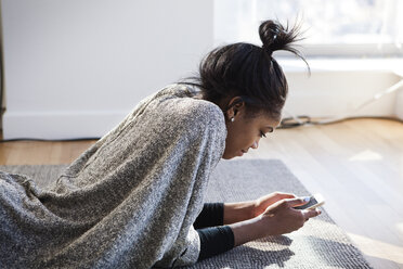 Woman using mobile phone while lying on floor at home - CAVF07966