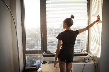 Rear view of woman standing by window at home - CAVF07973