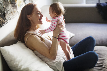 Mother playing with daughter while sitting on sofa at home - CAVF07979