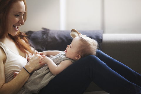 Abgeschnittenes Bild der Mutter, die einem kleinen Mädchen die Haare bürstet, während sie zu Hause auf dem Sofa sitzt, lizenzfreies Stockfoto