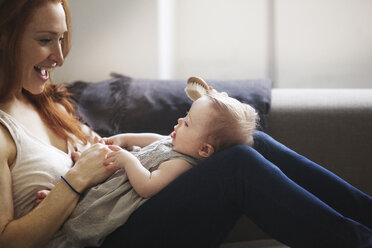 Abgeschnittenes Bild der Mutter, die einem kleinen Mädchen die Haare bürstet, während sie zu Hause auf dem Sofa sitzt - CAVF07995