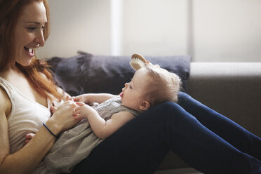 Cropped image of mother brushing baby girl's hair while sitting on sofa at home - CAVF07995