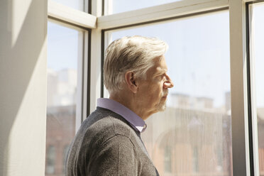 Seitenansicht eines älteren Mannes, der durch das Fenster seines Hauses schaut - CAVF08058