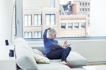 Frau mit Buch auf Sofa sitzend zu Hause - CAVF08067