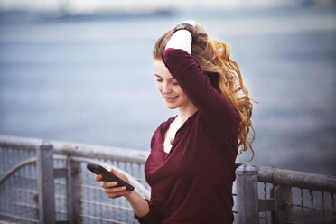 Woman with hand in hair using smart phone against river - CAVF08124