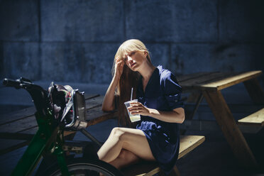 Woman looking while sitting on bench in city - CAVF08139