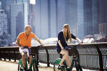 Cheerful couple cycling by railing against buildings - CAVF08146