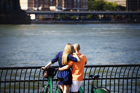 Rückansicht eines Paares mit Fahrrädern, das am East River steht - CAVF08148