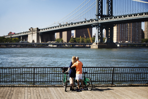 Rückansicht eines Paares mit Fahrrädern vor der Manhattan Bridge, lizenzfreies Stockfoto