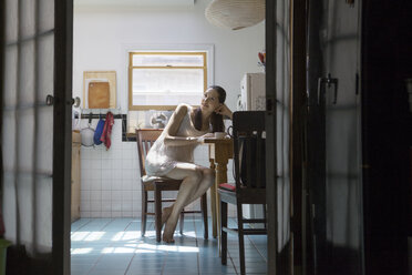 Pregnant woman looking away while sitting on chair in kitchen - CAVF08169