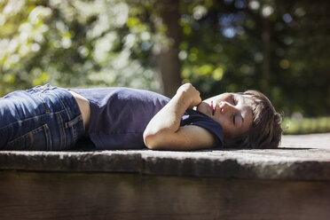 Boy sleeping on porch in sunlight - CAVF08178