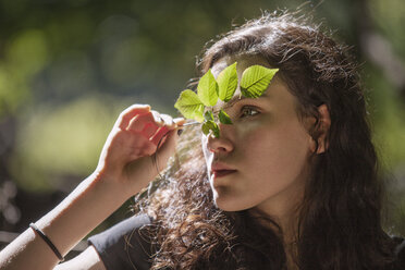 Teenage girl looking away while holding plant stem - CAVF08182