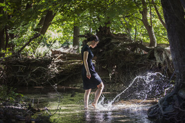 Teenager-Mädchen spritzt Wasser, während sie in einem Bach im Wald steht - CAVF08188