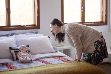 Seitenansicht einer glücklichen Frau mit Blick auf ein fröhliches kleines Mädchen, das zu Hause auf dem Bett liegt - CAVF08232