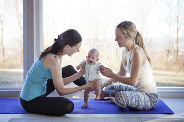 Cheerful homosexual females playing with baby girl on exercise mat at home - CAVF08240