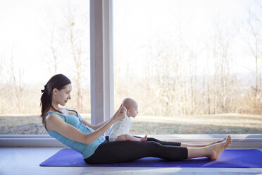 Seitenansicht einer Frau, die Yoga praktiziert und ein kleines Mädchen am Fenster hält - CAVF08241
