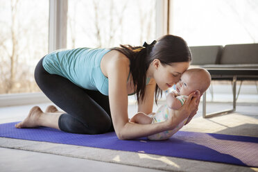 Loving mother holding baby girl while kneeling on exercise mat - CAVF08246