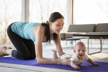 Happy mother holding baby girl while kneeling on exercise mat - CAVF08247