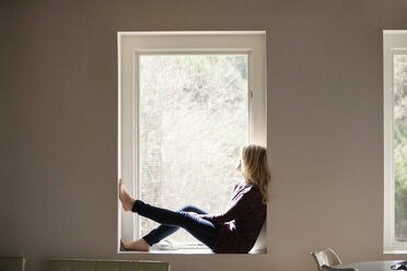 Seitenansicht einer nachdenklichen Frau, die zu Hause auf der Fensterbank sitzt - CAVF08266