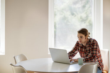 Man using laptop at table by window - CAVF08271