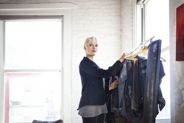 Thoughtful woman choosing clothes from rack at home - CAVF08304
