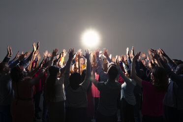 Diverse crowd with arms raised around bright light - CAIF16218