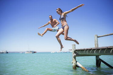 Couple jumping off wooden dock into water - CAIF16271