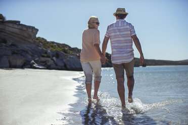 Couple holding hands walking along shore - CAIF16275