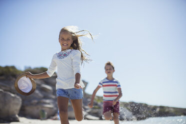 Young girl and boy running along beach - CAIF16288