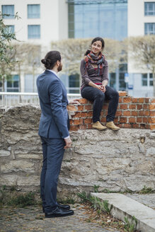Woman sitting on a wall outside office building smiling at businessman - JSCF00067