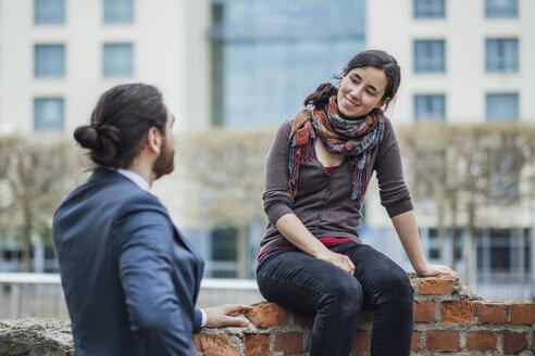 Woman sitting on a wall outside office building smiling at businessman - JSCF00068