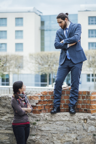 Businessman standing on a wall looking down at woman stock photo