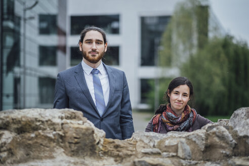 Portrait of businessman and woman behind a wall outside office building - JSCF00072