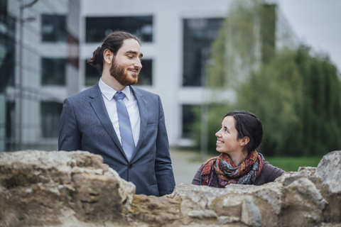 Smiling businessman and woman behind a wall outside office building stock photo