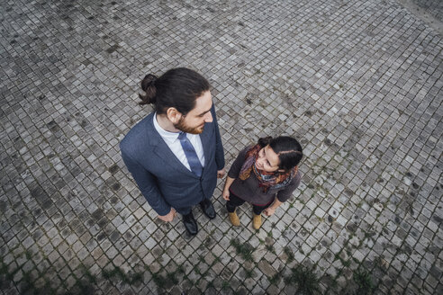 Woman and businessman standing on cobblestones smiling at each other - JSCF00076