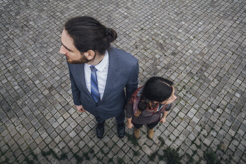 Woman and businessman standing on cobblestones looking in opposite directions - JSCF00078