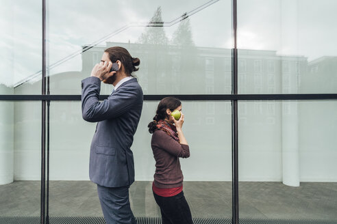 Businessman talking on cell phone with woman holding an apple at her ear - JSCF00081