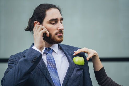 Businessman talking on cell phone and woman placing an apple in his jacket pocket - JSCF00083